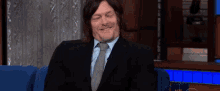 a man in a suit and tie is sitting on a blue couch talking to someone .