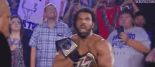 a wrestler is holding a championship belt in front of a crowd .