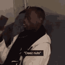 a man is sitting on a couch holding a cell phone in his hand and says `` deez nuts '' .