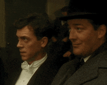 a man in a tuxedo and a man in a hat sit next to each other
