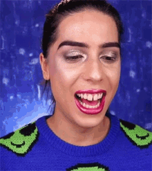 a woman wearing a blue and green sweater with smiley faces on it is making a funny face .