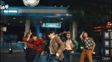 a group of people are dancing in front of a gas station sign