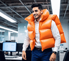 a man wearing an orange vest is standing in front of a computer