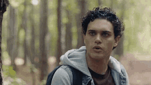 a young man with a backpack is standing in the woods .