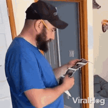 a man with a beard wearing a blue shirt and a black hat is looking at a book .