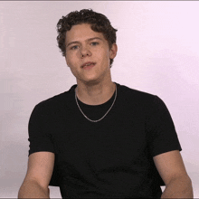 a young man with curly hair wearing a black shirt and a silver chain around his neck