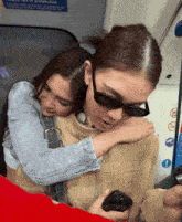 a woman wearing sunglasses is hugging another woman wearing a syfuel jacket