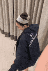 a woman wearing a blue hoodie that says ' memories ' on the back is standing in front of a curtain .