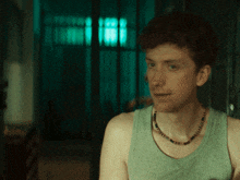 a man wearing a tank top and a beaded necklace looks at the camera