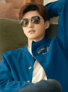 a man wearing sunglasses and a blue jacket with the word savor embroidered on it