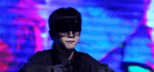 a man wearing a black hat and sunglasses is standing in front of a blue and purple background .