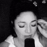 a black and white photo of a woman singing into a microphone with her eyes closed .