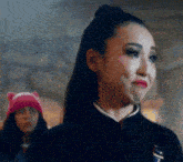 a woman in a black jacket is making a funny face while a woman in a pink hat is standing behind her .