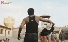 a man in a black tank top is walking down a street with a group of people behind him .