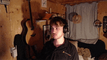 a man wearing headphones in a room with a guitar and a skateboard