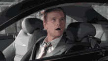a man in a suit and tie is driving a car with his mouth open