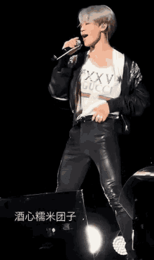 a man is singing into a microphone on a stage while wearing leather pants .