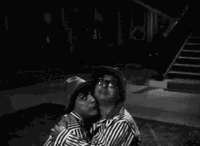 a black and white photo of a man in a striped shirt standing next to a woman .