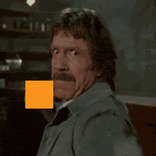 a man with a mustache is standing in front of an orange square that says " eh t this "