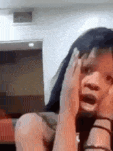 a woman is sitting on a couch with her hands on her face .