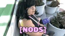 a woman sitting in front of potted plants with the words [ nods ] written in pink