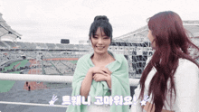 a girl wrapped in a green blanket stands next to another girl with red hair