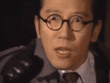 a close up of a man wearing glasses and a tie making a surprised face .