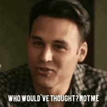 a man in a plaid shirt is sitting at a table and talking to someone .