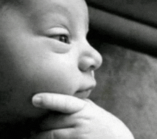 a black and white photo of a baby 's face with a hand on its chin .