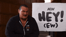 a man sitting in front of a sign that says hey ew