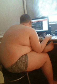 a man without a shirt is sitting at a desk in front of a computer monitor