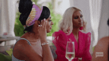 two women are sitting at a table with wine glasses and talking .