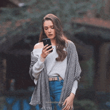 a woman wearing a sweater and a scarf is looking at her phone