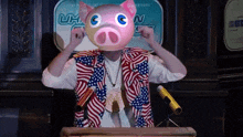 a man wearing a pig mask stands at a podium in front of a sign that says uhn