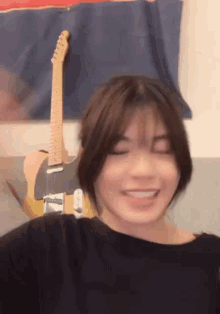 a woman is smiling in front of an electric guitar .