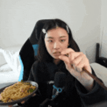 a woman is eating noodles with a spoon while sitting in a chair .
