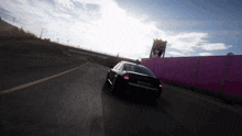 a black car driving down a road with a pink wall in the background