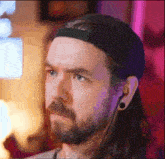 a man with long hair and a beard wearing a hat and ear plugs .
