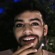 a man with a beard is smiling with his hand to his mouth