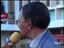 a man wearing glasses is talking into a microphone with the number 3 on it .