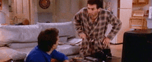 two men are standing next to each other in a living room . one of the men is wearing a robe .