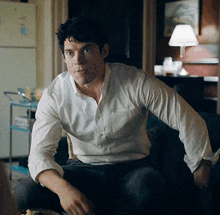 a man in a white shirt is sitting on a couch in front of a refrigerator