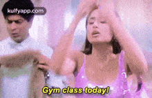 a woman in a purple top is dancing in a gym while a man looks on .