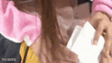 a woman wearing a pink sweater and a yellow shirt is holding a piece of paper .