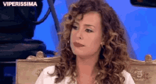 a woman with curly hair is sitting in a chair with a camera in the background .