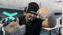 a man wearing headphones giving a thumbs up in front of a green x