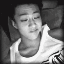 a black and white photo of a young man in a white tank top sleeping .
