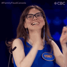 a woman wearing glasses and a blue dress has a name tag that says sydney