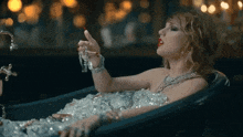 a woman is laying in a bathtub covered in ice and holding a lipstick .