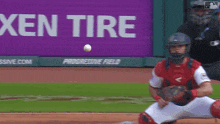 a baseball catcher catches a ball in front of a xen tire sign